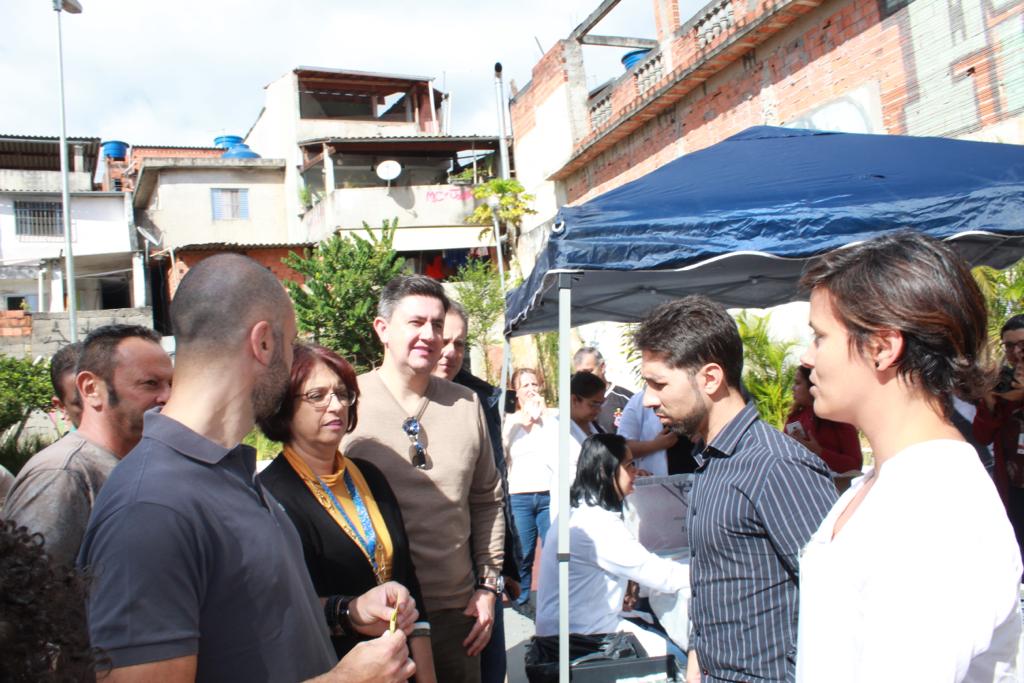 Na foto está o prefeito Bruno Covas e o presidente da Cohab Alexsandro Peixe, ambos ao lado esquerdo conversando com mutuários e representantes da Cohab. 