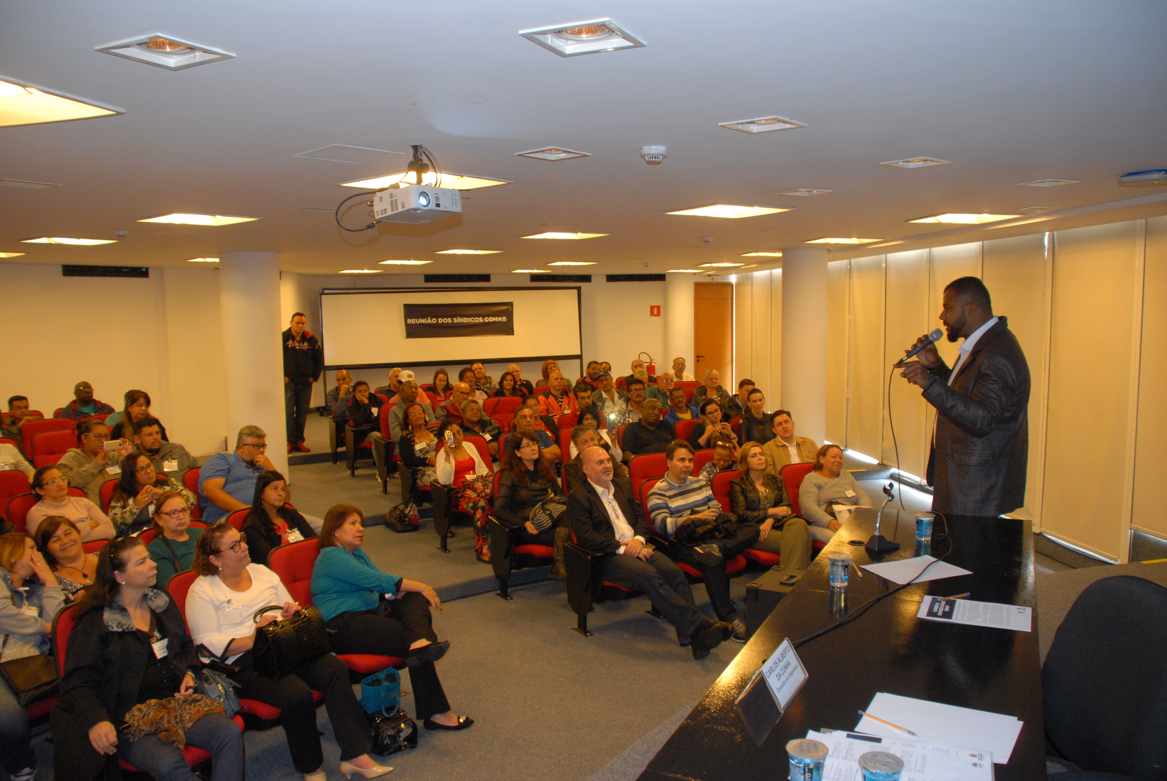 Foto de cima do palco, onde o delegado titular do DEIC, Carlos Alberto da Cunha à direita falando com a plateia de frente
