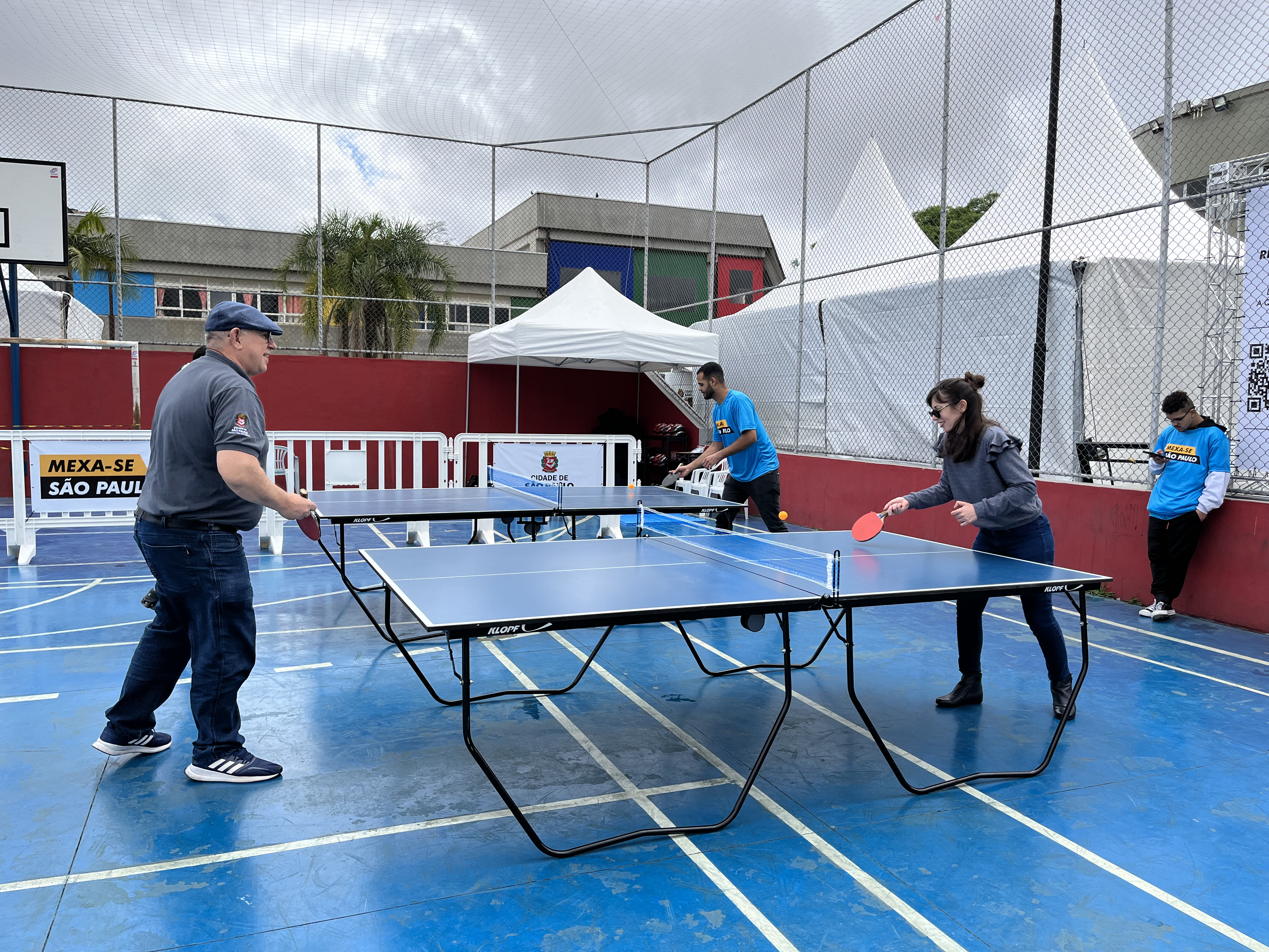 Três pessoas aparecem na foto jogando em uma mesa de ping pong 