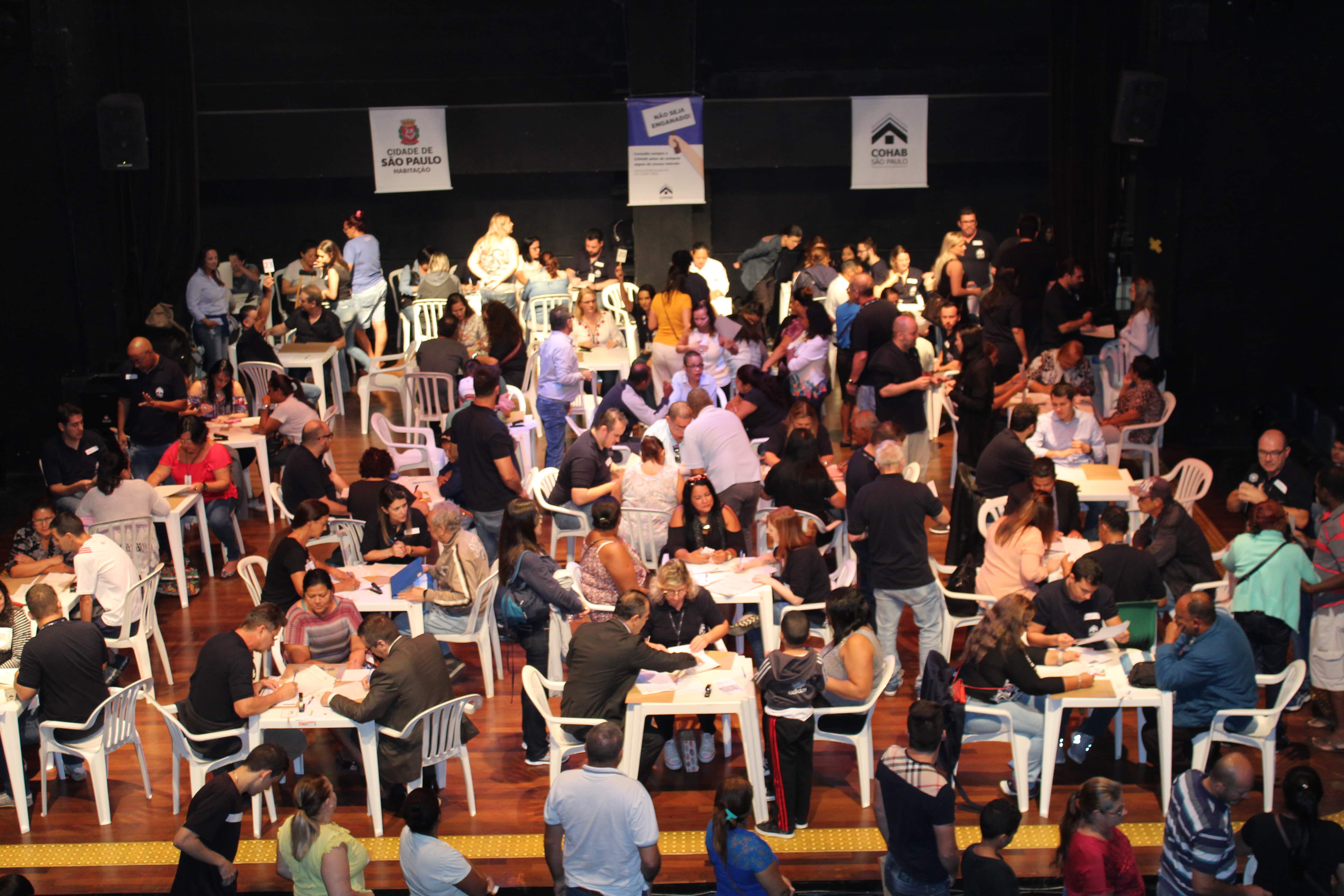Imagem vista de cima de diversas mesas de atendimento dentro do teatro do CEU Água Azul