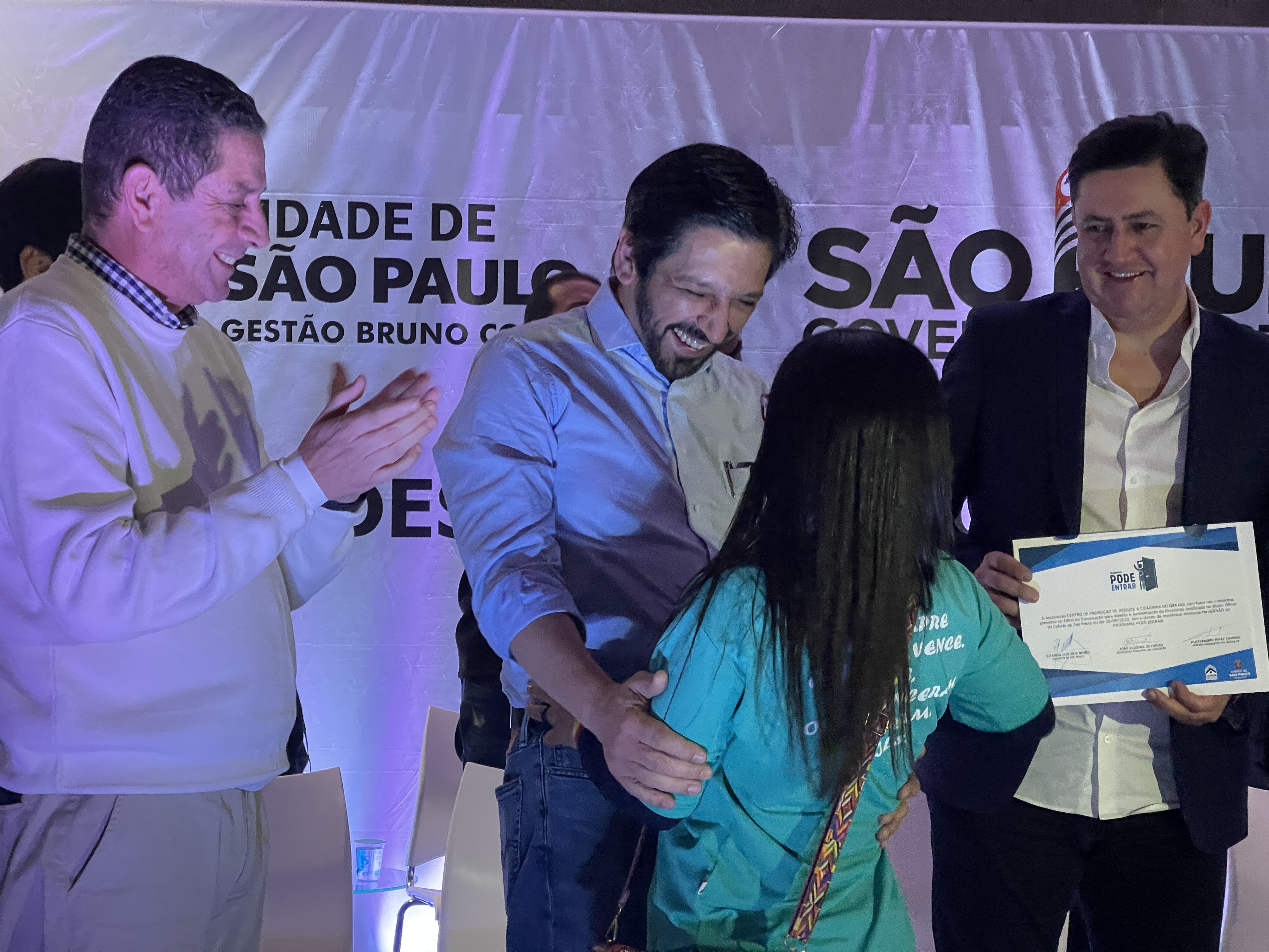 Prefeito Ricardo Nunes, Secretário João Farias e o Presidente da Cohab-SP Alex Peixe, entregam o certificado à representante de uma das entidade. 