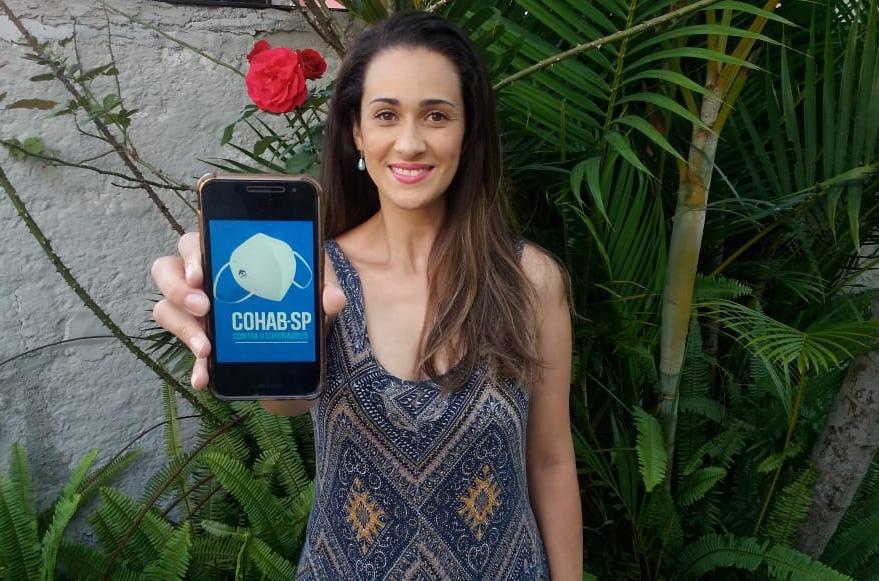 A síndica e moradora do Conjunto Habitacional Adventista posa para a foto sorrindo e mostra a tela de um celular com a imagem “Cohab-SP Contra o Coronavírus”.