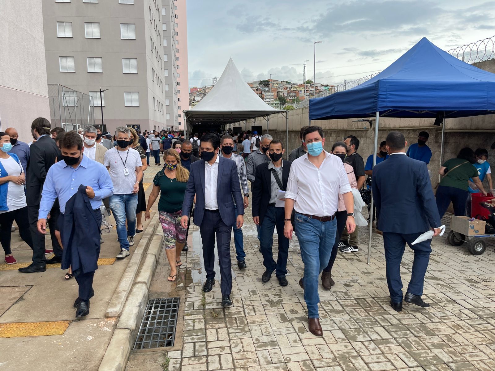Na foto o prefeito caminha seguido por uma moradora e outras autoridades, como o secretário de habitação, João Farias, e o presidente da Cohab, Alex Peixe.