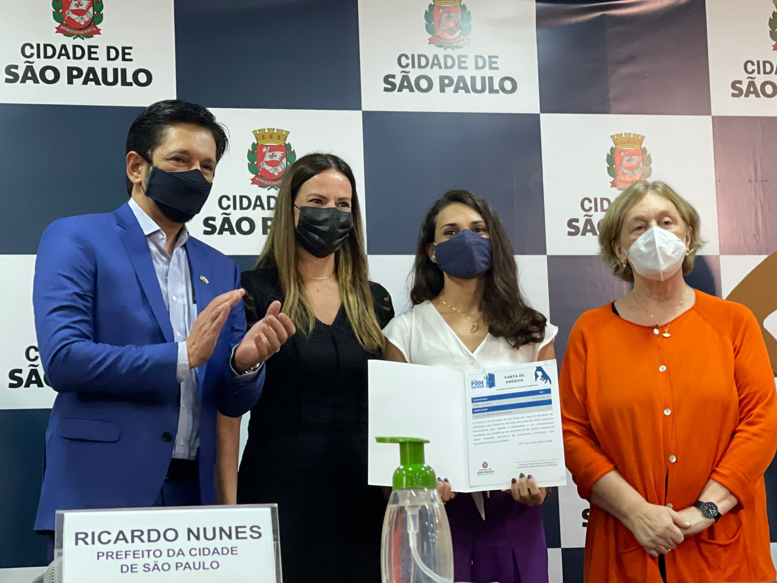 Prefeito de São Paulo Ricardo Nunes com autoridades batendo palmas para as mulheres que serão beneficiadas com as cartas de crédito