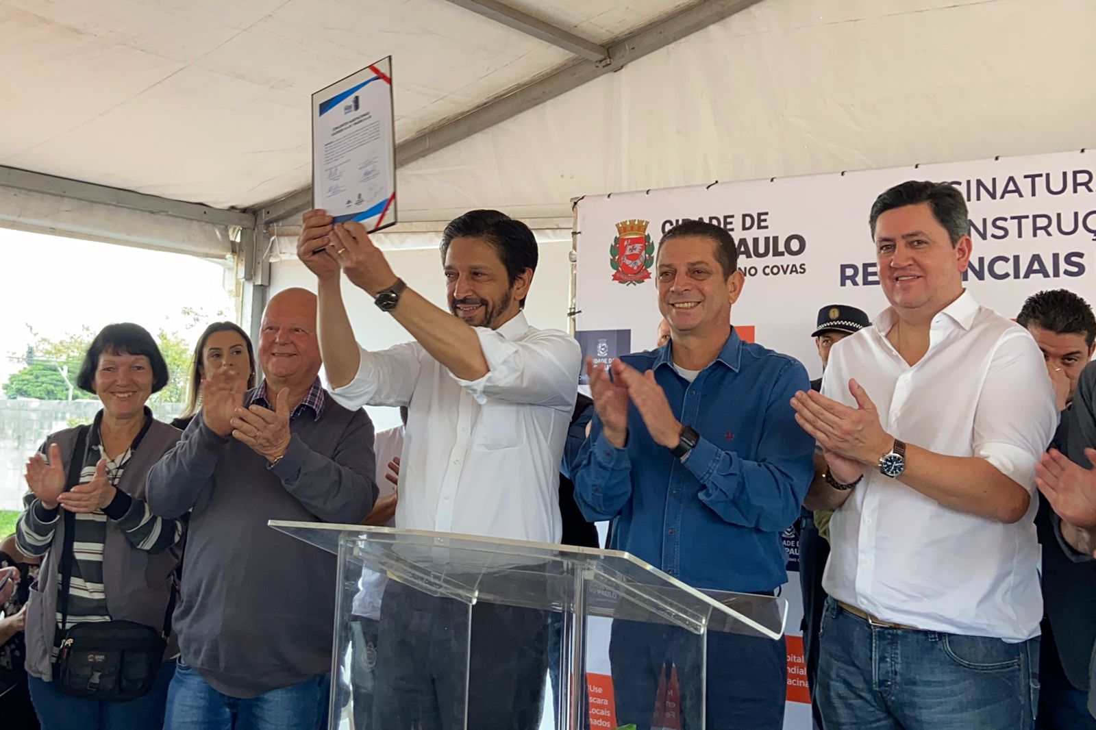 Prefeito de São Paulo Ricardo Nunes, no centro da foto, ergue o documento com as assinaturas que oficializam o início das obras de moradia. 