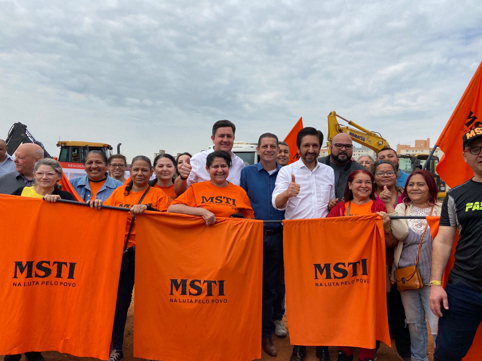 Prefeito de São Paulo Ricardo Nunes, Presidente da Cohab, Alex Peixe e o Secretário Municipal de Habitação João Farias posam junto com membros do movimento MSTI que estão de camisas laranjas.