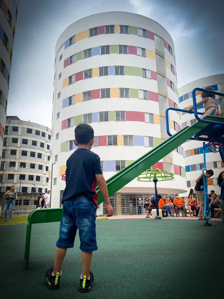 Com prédios ao fundo, criança brinca em brinquedo da área comum do empreendimento.