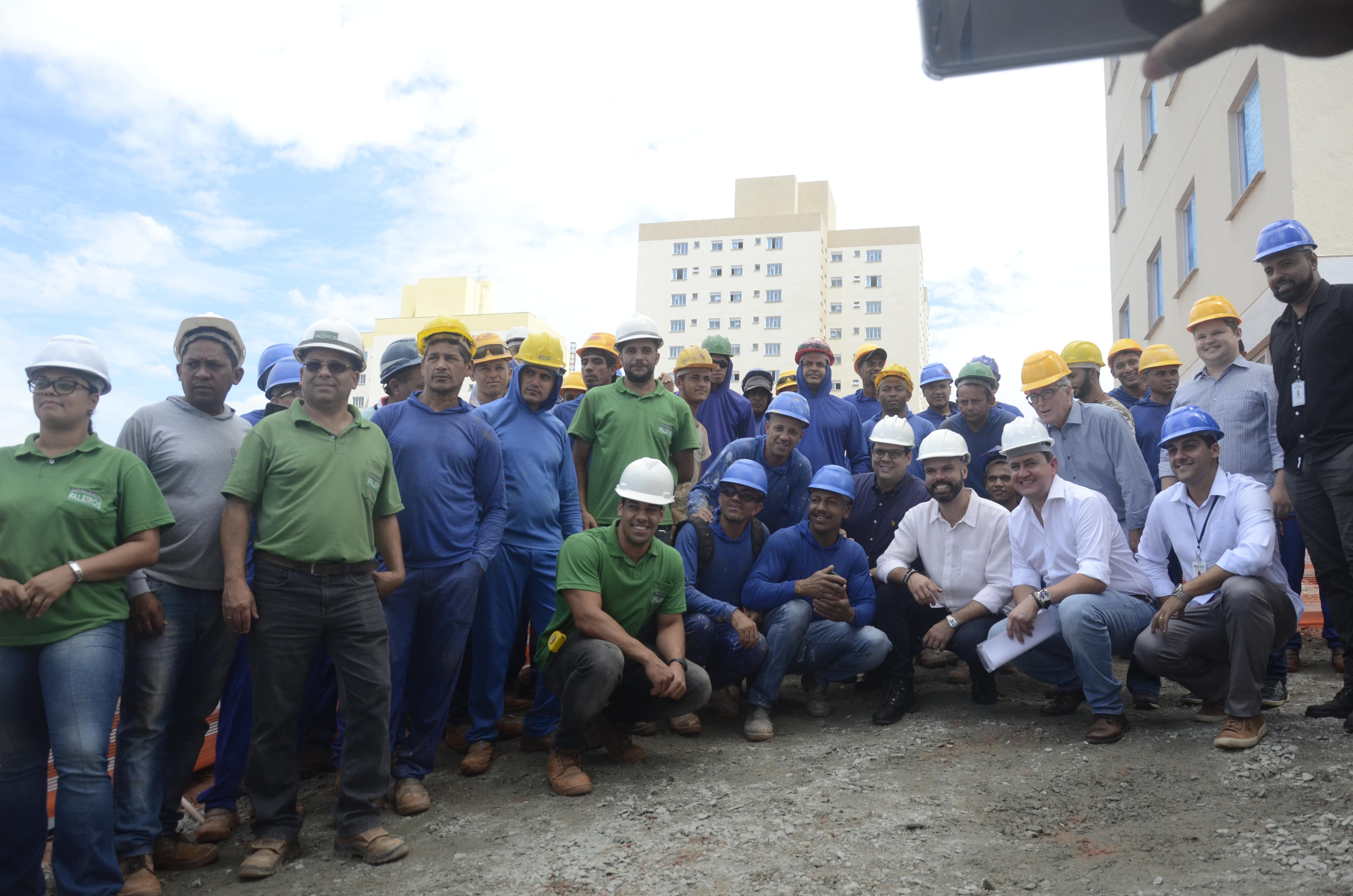 O Prefeito de São Paulo Bruno Covas e Presidente da Cohab Alexsandro Peixe posam junto aos trabalhadores da obra. Tem cerca de 20 trabalhadores de pé alguns usando verde azul ou cinza.